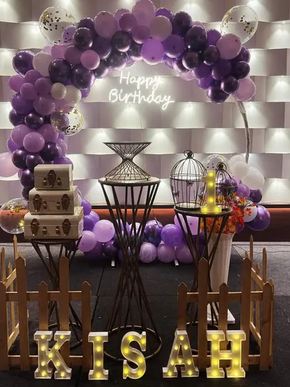 A closer view of the purple-themed first birthday, highlighting the vintage-style suitcases and the soft lighting.