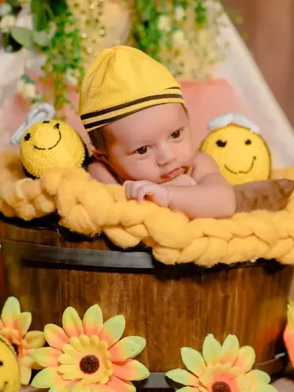 A sweet close-up of a newborn in a bucket, surrounded by smiling crochet bee props and sunflowers.