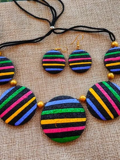 A bold necklace featuring round terracotta pendants with multi-colored stripes. The textured surface adds depth to this modern, graphic piece.
