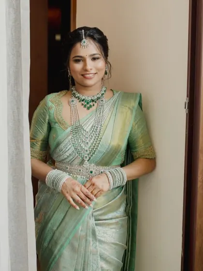 A bride in a beautiful pastel green Kanchipuram saree. Her custom blouse features a unique scalloped neckline and detailed embroidery, perfectly matching her diamond and emerald jewelry.