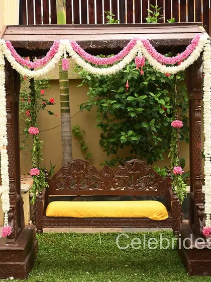 A traditional wooden swing (oonjal) decorated with jasmine and pink flowers, perfect for a baby shower or engagement ceremony in a garden setting.