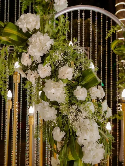 A detailed look at a floral arrangement on a modern arched backdrop. The combination of white hydrangeas, baby's breath, and green foliage against a curtain of crystal beads showcases our attention to detail.