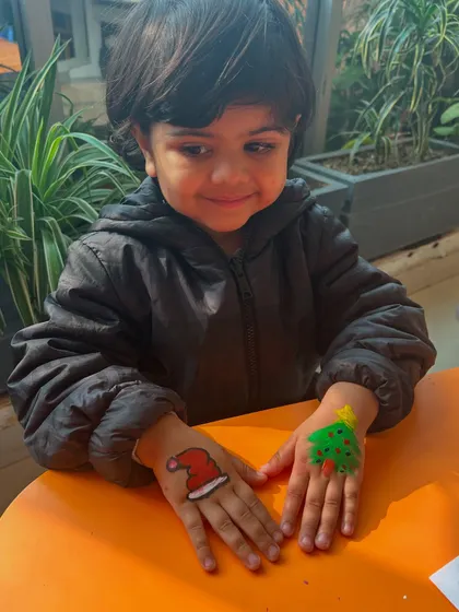A boy proudly shows off his festive hand paintings of a Santa hat and a Christmas tree.