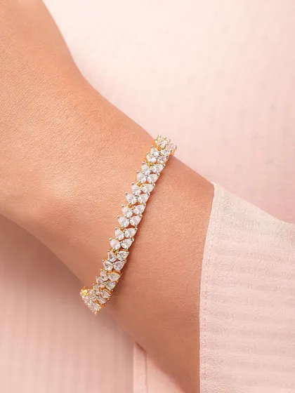 A close-up of a diamond bracelet on a model's wrist. The soft pink background complements the gold and diamonds, creating an elegant and feminine look.