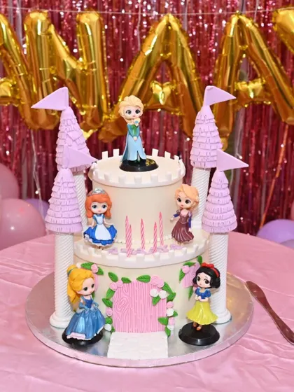 A fairytale Disney Princess castle cake. This two-tiered design features towers and beloved princesses like Elsa, Snow White, and Cinderella, creating a magical centerpiece.