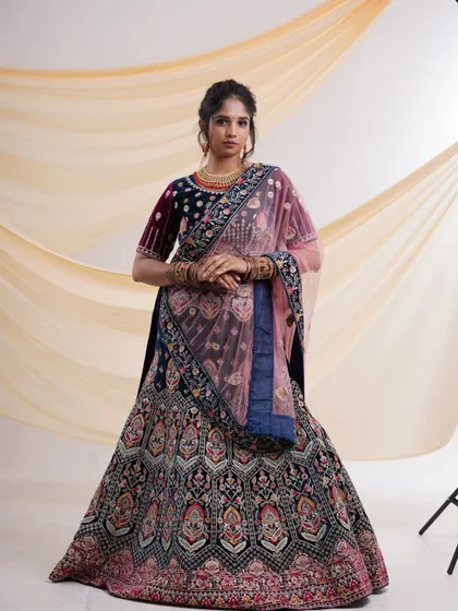 A full-length view of an exquisite navy blue velvet lehenga with intricate multi-color embroidery and a contrasting pink dupatta. This is a perfect rental for a wedding or reception.