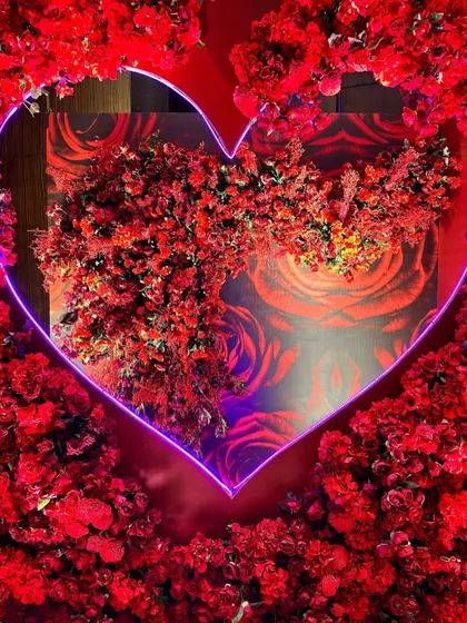 A love-themed photo booth featuring a large heart-shaped neon light framing a wall of red roses, creating a passionate and modern backdrop.