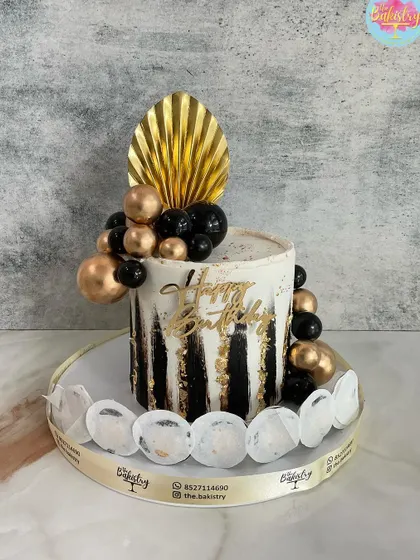 An elegant black, white, and gold cake with a fan topper and decorative spheres.