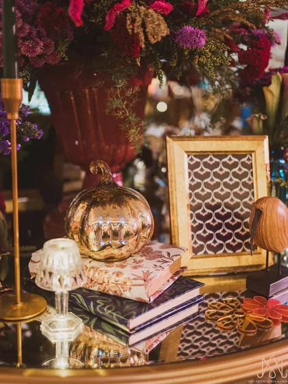 An artful arrangement of decorative objects on a mirrored table, including a metallic pumpkin, a wooden bird, and vintage-style books.