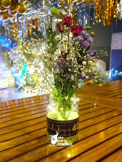 A close-up of a table centerpiece from the blue and gold 40th birthday, featuring a jar of wildflowers illuminated from within by fairy lights for a magical touch.