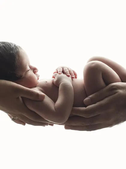 A classic "in your hands" newborn pose, showing the baby resting peacefully in the hands of their parents. The high-key lighting creates a pure and timeless feel.