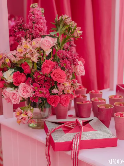 A close-up of the pink-themed decor, featuring beautiful floral arrangements, word games for guests, and traditional Indian sweets (mithai) in custom boxes.