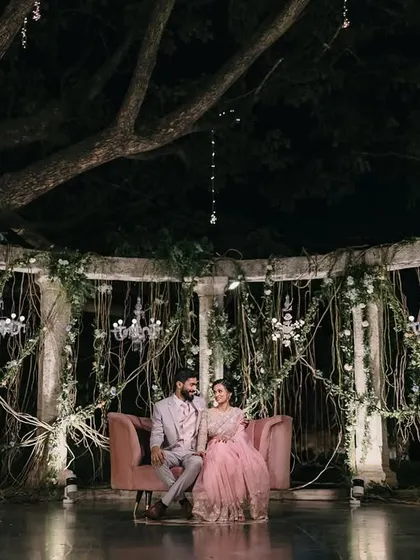 We created an enchanted forest theme for this reception stage, using natural vines, chandeliers, and a cozy pink sofa to craft a whimsical and romantic setting.