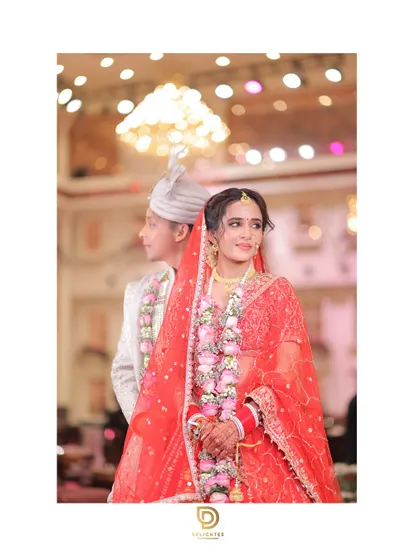 A beautiful portrait of the bride in her red lehenga, with the groom slightly out of focus behind her, creating an artistic shot that highlights her as the star of the moment.