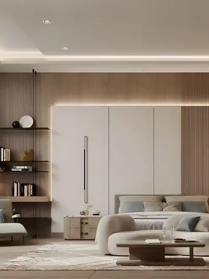 A serene and spacious bedroom with a sitting area. The design uses a neutral color palette, integrated cove lighting, and built-in shelving to create a calm and functional retreat.