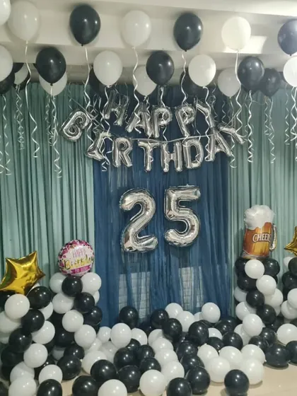 A black and white themed room decoration for a 25th birthday. This setup includes balloon pillars, ceiling balloons, and a curtain backdrop for a chic and modern party at home.