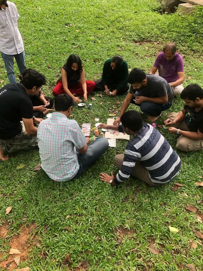 A group gathered in a circle on the grass, engaged in a collaborative art activity.