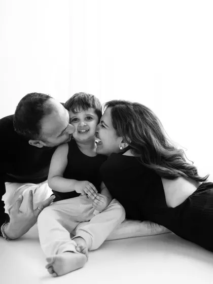 The beauty of black and white photography lies in its ability to focus on pure emotion. This image is filled with love and laughter, as parents shower their son with kisses, creating a powerful and timeless family portrait.
