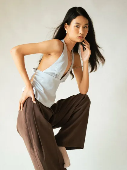 A dynamic, full-body pose in a studio setting. This shot captures a sense of movement and confidence, showcasing the entire outfit from the halter top to the wide-leg trousers.