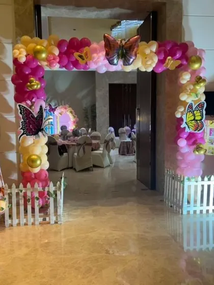 An enchanting butterfly-themed entrance arch for a birthday party, made with pink and yellow balloons and decorated with large butterfly cutouts.