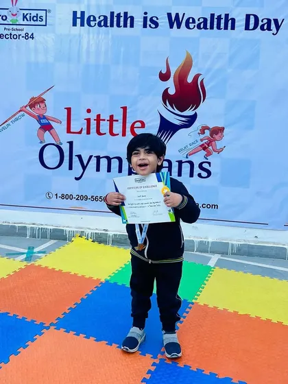 Celebrating every participant. A happy student shows off his medal and certificate in front of our 'Little Olympians' banner, beaming with a sense of accomplishment.