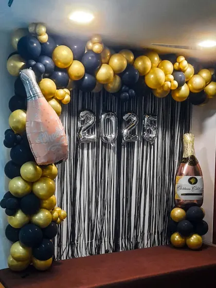 Our New Year backdrop pairs black and gold balloons with champagne-bottle foils, silver tinsel and "2025" lettering.