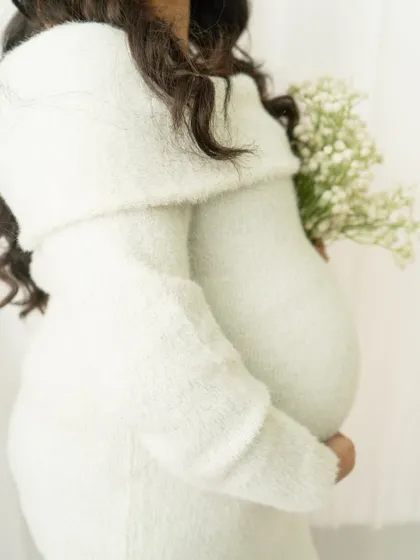 A close-up detail shot focusing on the baby bump and the soft texture of a cozy sweater dress. It's a simple, intimate, and beautiful portrait.