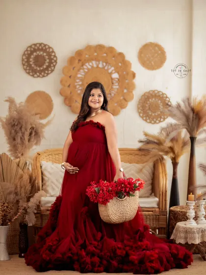 A joyful solo portrait of a mom-to-be in a magnificent red ruffled gown, surrounded by our boho studio decor.
