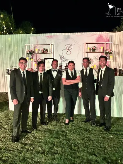 The Tipsy Co team in sharp black suits, standing in front of an elegant, custom-monogrammed bar. We pride ourselves on a team that looks as good as the drinks they make.