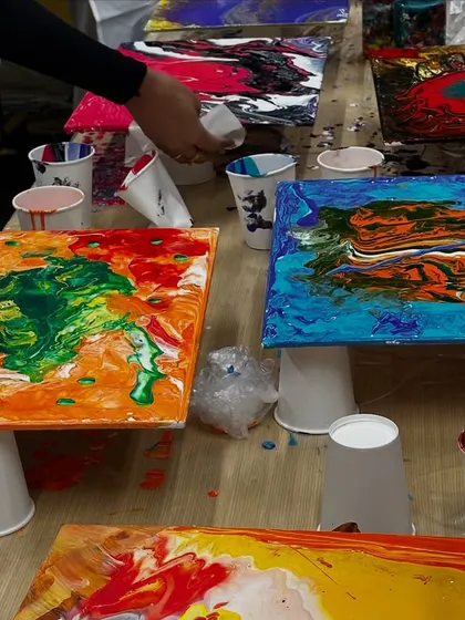 A table full of vibrant, wet fluid art paintings. Each canvas is completely unique, reflecting the colors and movements chosen by its creator.