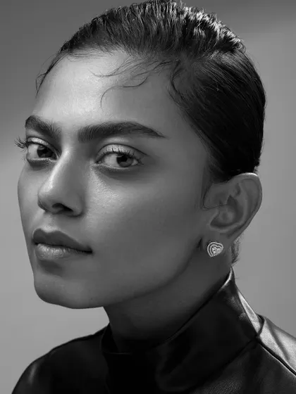 A powerful and direct portrait showcasing elegant diamond studs. The minimal styling and clean background ensure the luxury product is the hero of the image.
