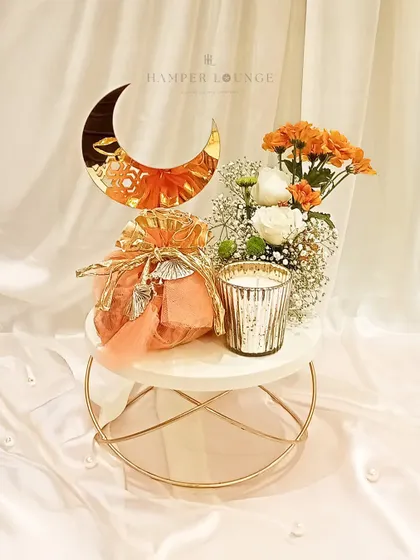 Simple, elegant, and perfect for a smaller gesture. This Eid gift features a treat-filled potli bag and a mercury glass candle set upon a stylish marble and gold stand, accented with a golden moon and fresh flowers.