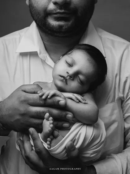 A detailed black and white close-up of a newborn's tiny feet and hands, held securely in their father's arms. A beautiful way to remember their perfect littleness.