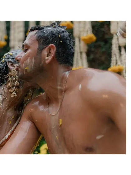 An intimate kiss shared between the couple amidst the messy, yellow-stained celebration of their Haldi.