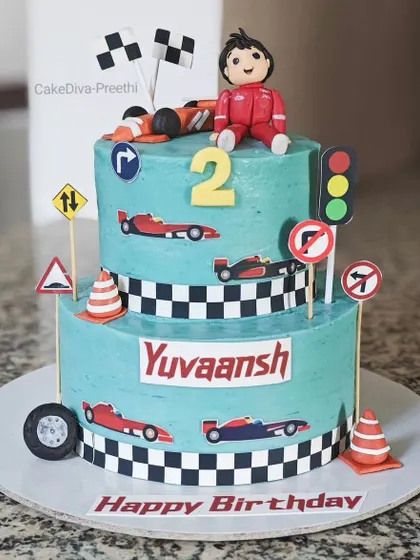 "Two Fast, Two Curious" is a fun theme for a second birthday. This two-tier red velvet ganache cake is decorated with race cars, traffic signs, and a checkered flag pattern to capture the speed and excitement.