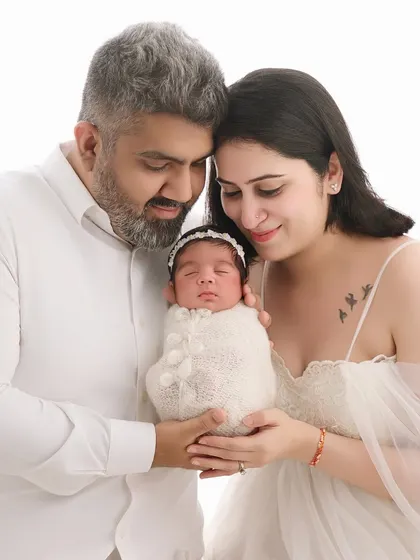 The same couple from our maternity gallery now holds their newborn daughter. Dressed in white against a clean background, this portrait beautifully continues their family's story, from anticipation to arrival.