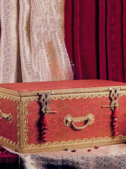 A close-up of the ornate red brocade sanduk, showcasing the detailed metalwork and tassels. This is a heritage piece, designed to be the highlight of your trousseau presentation.