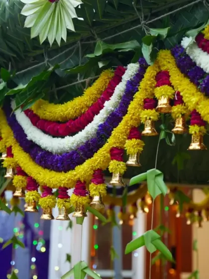 A close-up of a beautiful floral thoranam for a housewarming. This one is made with coconut leaves, colorful flowers, and small brass bells that jingle as guests arrive.