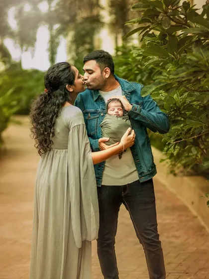 A beautiful family portrait where the father kisses the mother's cheek while she holds their newborn. This image, shot outdoors, is a testament to the love that blossoms with a new baby.