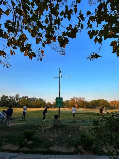A beautiful view of the range framed by trees, with golfers enjoying the clear blue sky.