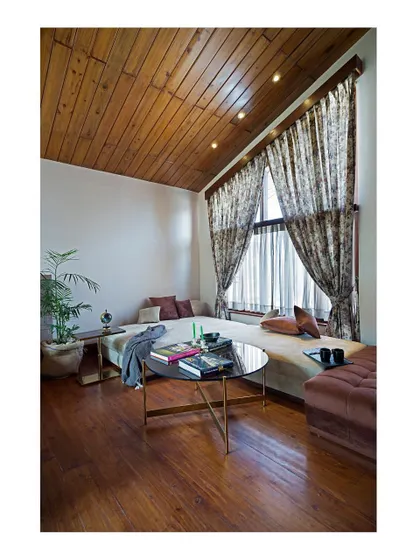 Another view of a sitting area within a bedroom, featuring a sloped timber ceiling that adds warmth and character. The space is arranged to maximize comfort and take advantage of the natural light from the large window.