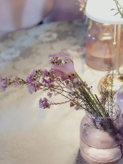 A detail shot of the delicate pink and purple flowers in a glass vase, illuminated by a table lamp.