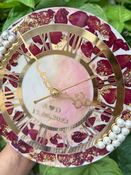 A delicate 10-inch clock featuring preserved red rose petals against a soft pink and white marbled background. The couple's initials and wedding date are subtly placed in the center.
