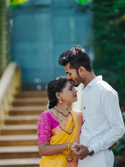 A tender pre-wedding moment with the groom-to-be kissing his partner's forehead. The traditional yellow saree looks beautiful.