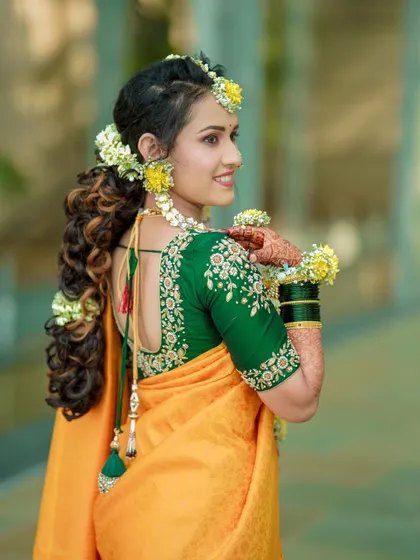 A beautiful profile shot of the bride during her Haldi ceremony, showcasing her intricate hairstyle and floral adornments.
