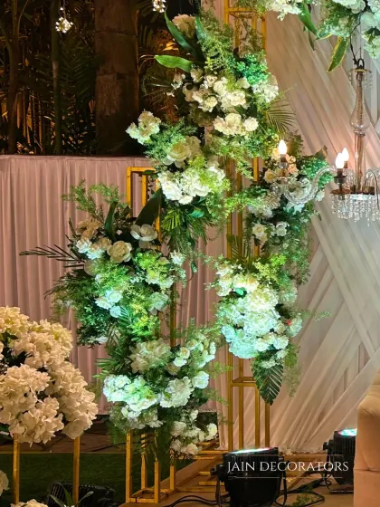 A close-up of a modern floral structure. White flowers and lush greenery are artfully arranged on a golden geometric frame, creating a piece that is both a floral arrangement and a sculpture.