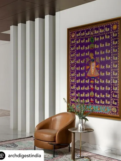 This is a traditional Pichwai painting, a beautiful piece of Indian heritage art that we incorporated into a modern setting. Placing it against a clean white wall with a simple leather armchair allows the artwork's intricate details and vibrant colors to truly shine.