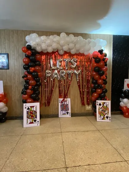 I can create fun, themed party setups like this casino or card party decoration. This design includes balloon pillars, a red tinsel curtain backdrop, 'LET'S PARTY' foil balloons, and large playing card props to complete the look.