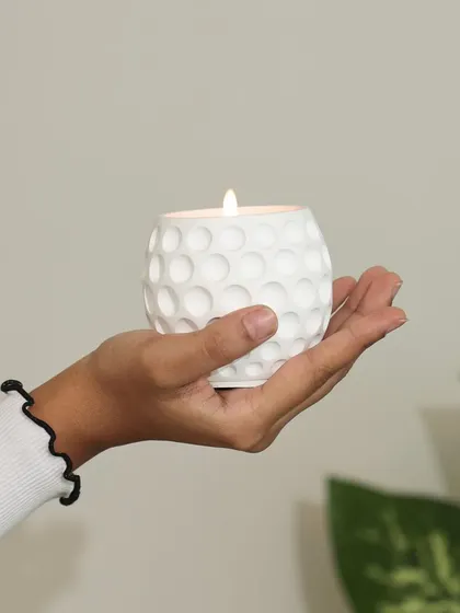 A hand holding our white scented candle with a golf ball texture. This piece is part of our minimal collection, designed to bring a touch of modern elegance and calm to your space.