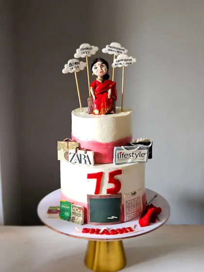 This two-tier cake was designed to celebrate a mother's 75th birthday by telling her life's story. It features a hand-sculpted figurine and edible toppers representing her career as a teacher, her love for shopping, and her journey through life.